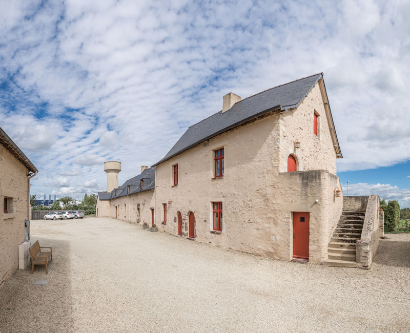 Maison de campagne avec une toiture en ardoise naturelle, de smurs preierres apparentes et des volets rouge.