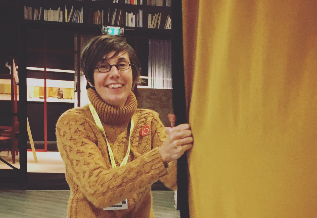 protrait de la designeuse et artiste julie gauthron. Elle porte un pull jaune et tire un rideau isolant phonique.