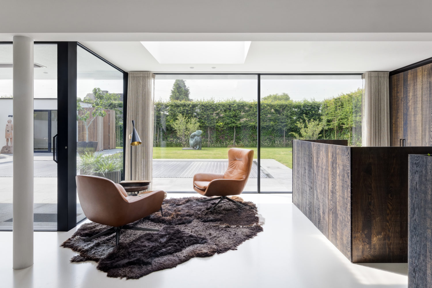 une jolie villa avec large baie vitreé qui donne sur une terrasse. Au premier plan deux fauteuils en cuir et un tapis au sol.e