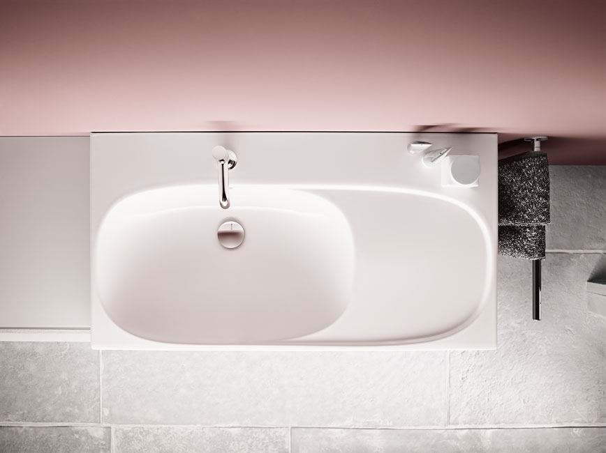 un lavabo aux belles formes arrondies et photographié du dessus. Il est posé contre un mur peint en rose.