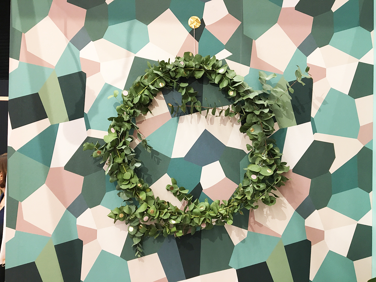 une couronne de noël toute simple accrochée su un papier peint très graphique rose, vert foncé et vert clair.