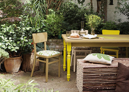 une terrasse aménagée avec une chaise en bois chinée, une table en bois aux pieds tournés et peints en jaune fluo. Peintures Julien