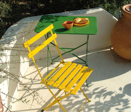 sur une terrasse inondée de soleil, une petite table en fer peinte en vert gazon et une chaise pliante en fer peinte en jaune fluo. Peintures Julien