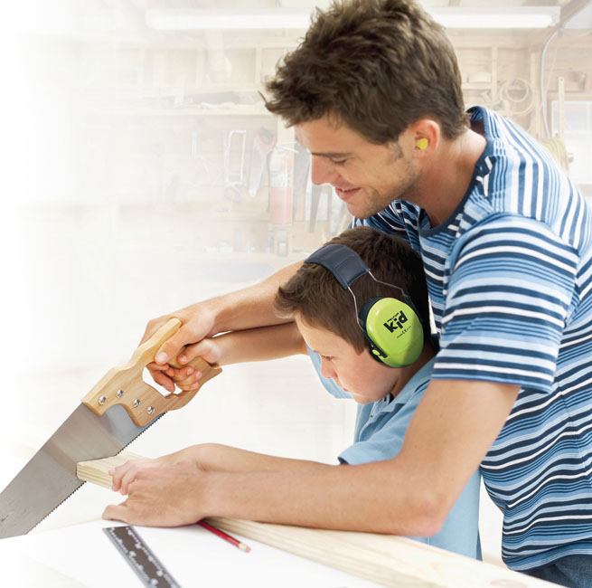 Un papa et son fils bricole ensemble. Ils scient une planche de bois. Le fils porte un casque anti-bruit