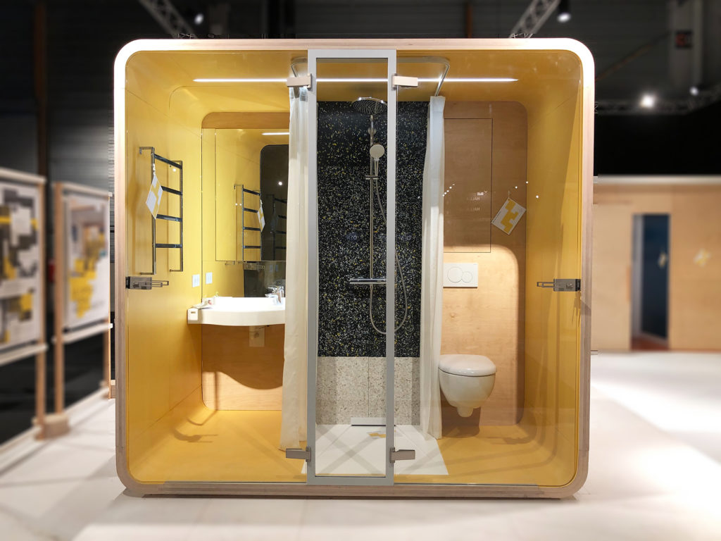 Exposiiton Vivre Bois. Une capsule comportant une salle d'eau complète est exposée au salon Architect@Work. Sa coque est en bois et l'intérieur est laqué jaune. Les sanitaires sont de marque Geberit.