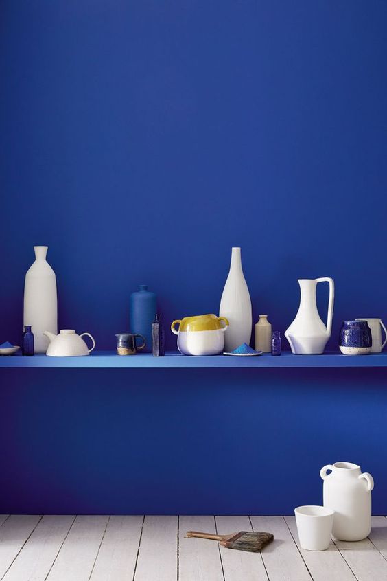 une étagère bleu sur un mur bleu offre un espace d'exposition à différents vases et pichets en céramique