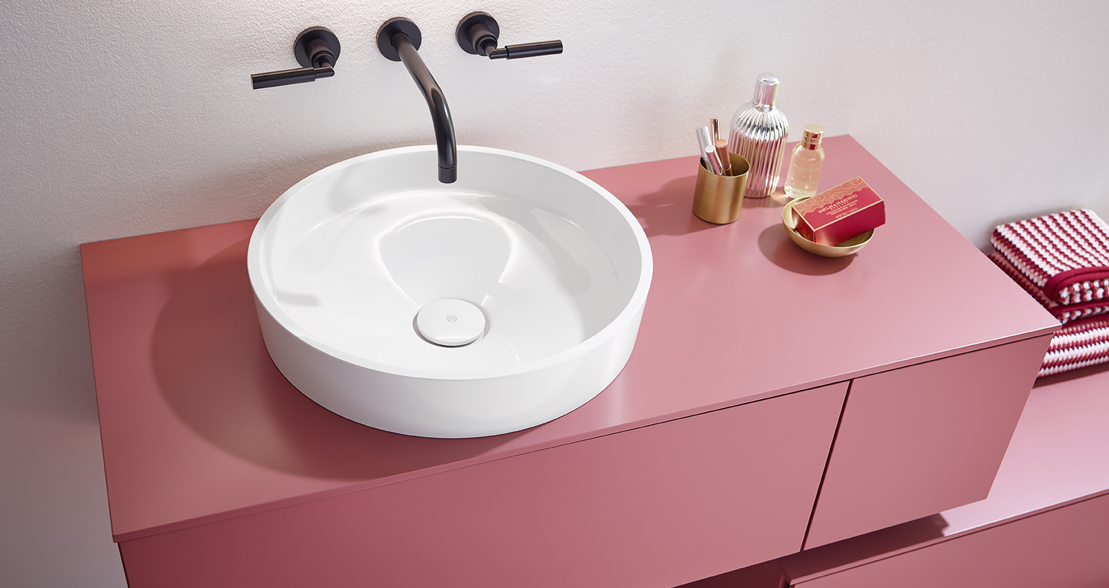 Une vasque ronde et blanche est posé sur un meuble de salle de bains rose framboise