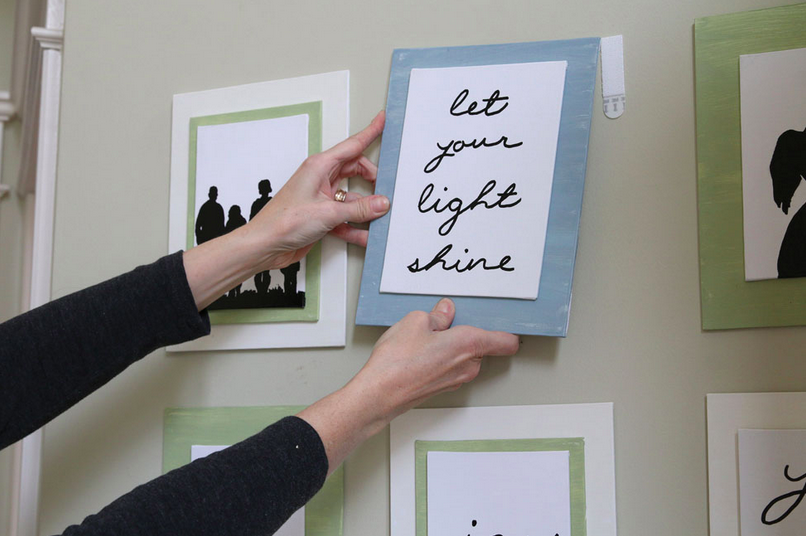 Des mains de femme positionne sur le mur un cadre contenant une calligraphie. Elle l'accorche avec les accroches tableaux Command