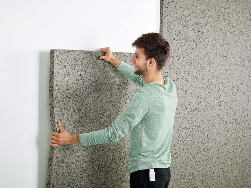 un jeune homme colle un panneau acoustique Silentwall sur un mur en plâtre