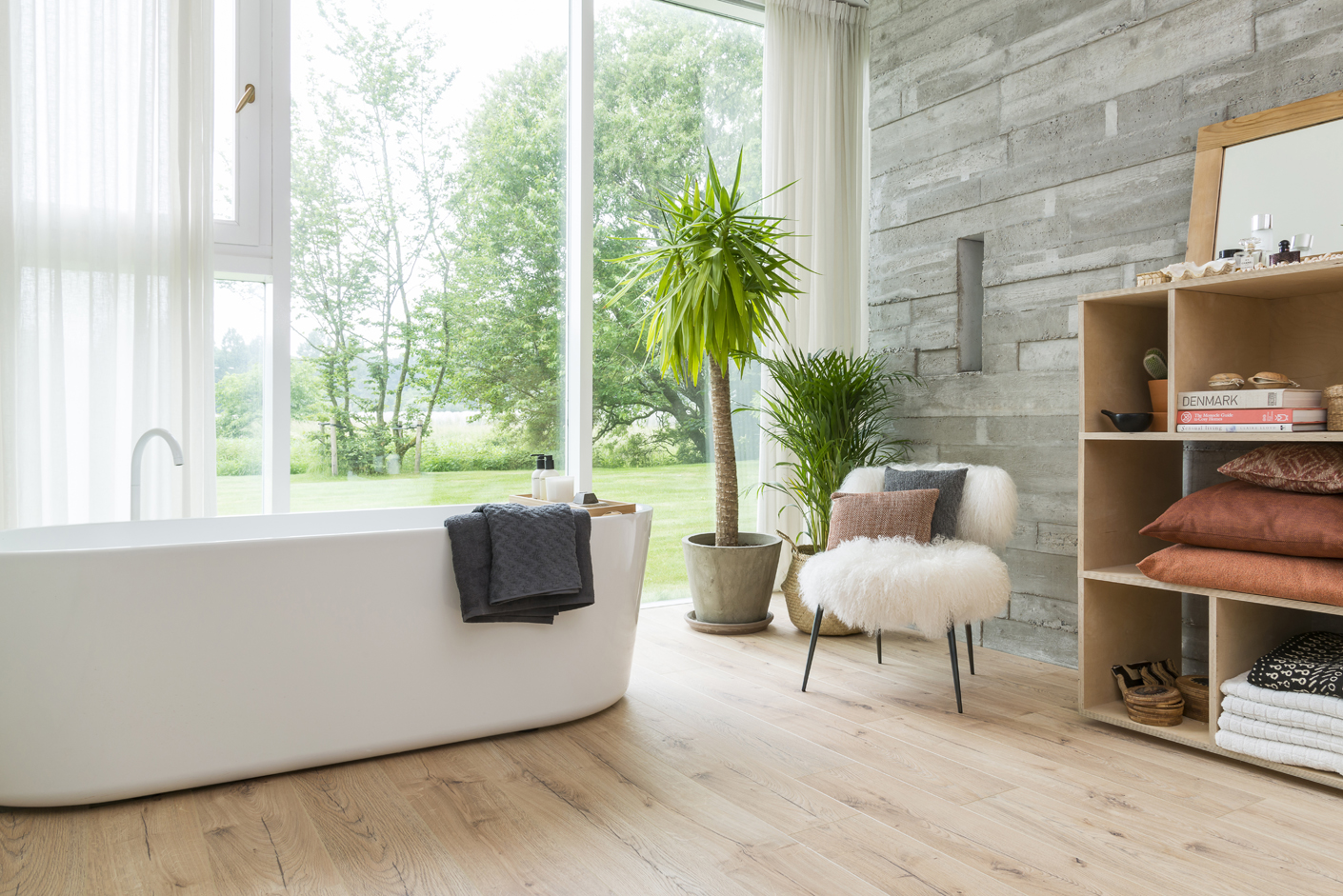 Une salle de bain inspire une qualité d'air intérieur saine avec sa vue sur un joli parc, sa baignoire immaculée et des plantes vertes sur un sol aspect bois clair.